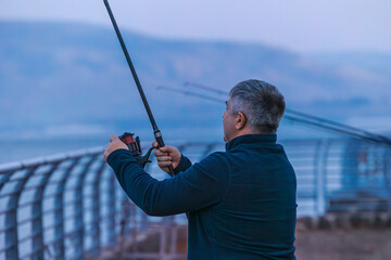 Man fishing on the Sea of Galilee waterfront. Back view, evening light, calm atmosphere, and...