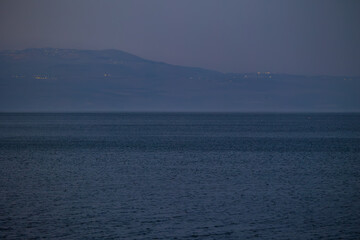 Obraz premium Evening twilight views of the Sea of Galilee in Israel with calm waters, distant mountains, boats, and serene blue tones creating a peaceful atmosphere