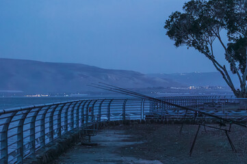 Wide angle photo of fishing rods on pier at Sea of Galilee in the evening, with calm water, distant...