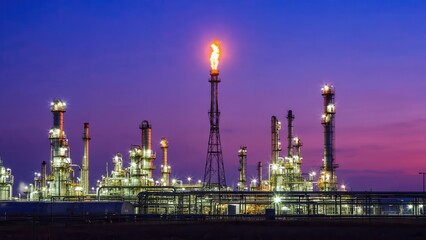 Fototapeta premium Gas flare burning over oil refinery at twilight