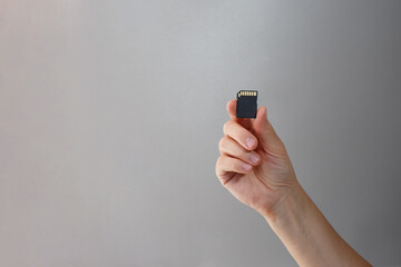 SD card in hand with gold contacts visible, on grey background for photography gear sellers, tech...