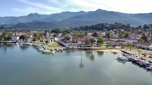 Aerial view of the historic colonial town of Paraty, a coastal gem in Rio de Janeiro, Brazil. Features the bay with boats, the Church of Santa Rita, and the Serra da Bocaina mountains.
