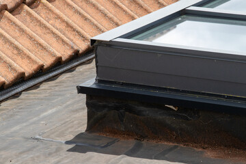 A modern skylight installation on a flat bitumen roof, showing the waterproofing and junction with an old clay tile roof
