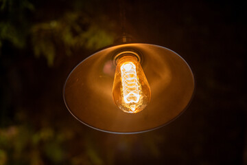 A close-up shot of a vintage-style light bulb illuminated within a metallic lampshade. The bulb...