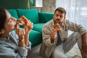 Couple enjoying pizza on living room floor: eating together at home