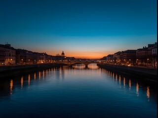 Obraz premium Scenic evening view of illuminated city riverfront with calm water reflections, glowing street lights, and beautiful twilight sky creating romantic and tranquil urban atmosphere