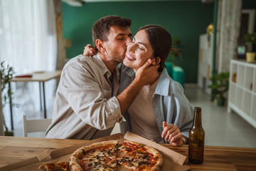 Happy couple kissing while enjoying pizza at home