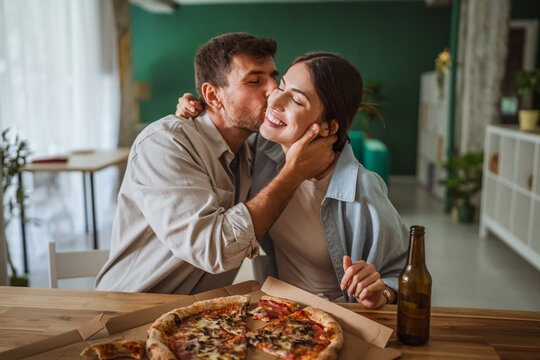 Happy couple kissing while enjoying pizza at home