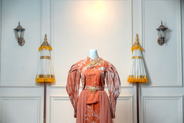 Elegant terracotta wedding gown on mannequin, featuring long puff sleeves, floral embroidery, gold...