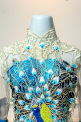 Close-up of an elegant blue gown with intricate peacock embroidery and lace collar, showcasing luxurious texture and craftsmanship for weddings, parties, and high-fashion events.