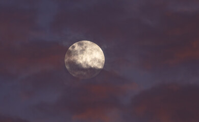 A full moon behind clouds in a sunset sky