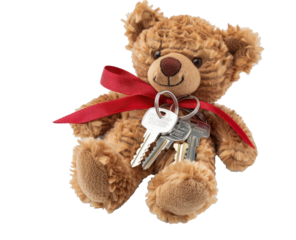 Small teddy bear holding house keys, red ribbon