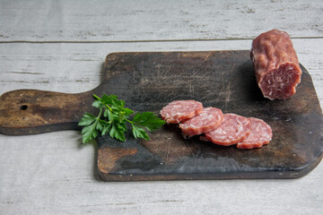 Smoked salami with parsley on a cutting board on a white wooden background