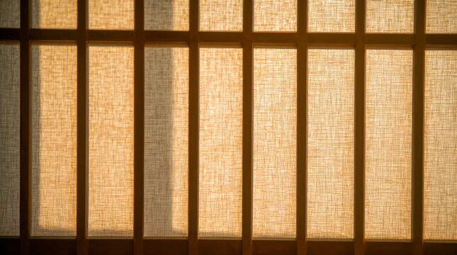 Warm sunlight filters through a textured, translucent paper screen divided by wooden mullions, creating a soft, serene ambiance and casting gentle shadows.