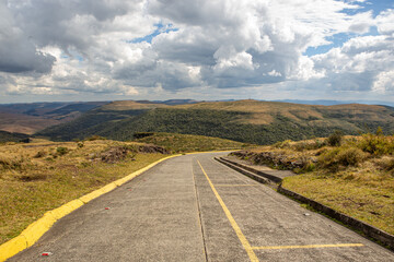 Estrada de asfalto com faixa amarela descendo por um vale na Serra Catarinense