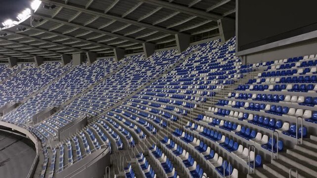 Aerial view drone flies over empty stadium or race track seats. Rows and blue and white seats without viewers and spectators. Evening shot of empty football stadium. Soccer Arena drone aerial view.