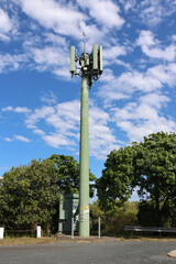 Telecommunications tower in front of trees with a blue sky with scattered white clouds
