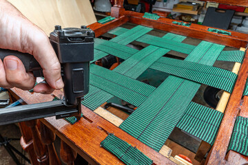 Upholsterer’s hand upholstering an armchair stapling strips of elastic webbing with a pneumatic stapler.