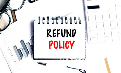 Notepad with text refund policy on desk with charts, keyboard, glasses and pen