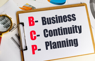 Clipboard with text business continuity planning on desk with charts and magnifying glass