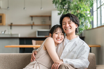 家のリビングでソファーに座る仲良しな若いアジア人夫婦
