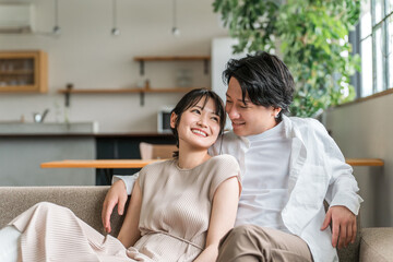 Fototapeta premium 家のリビングでソファーに座る仲良しな若いアジア人夫婦 