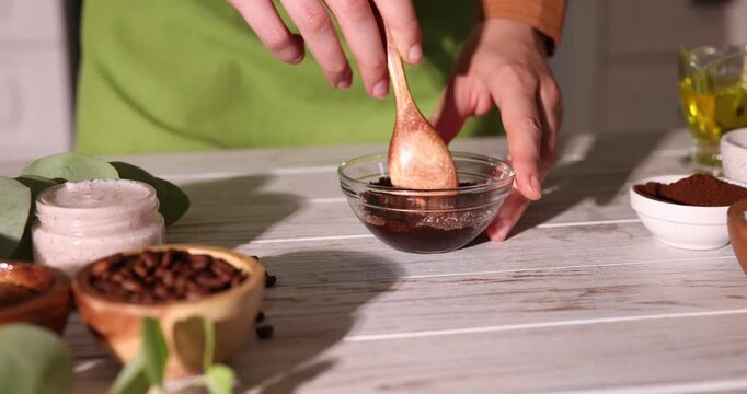 Making natural scrub. Woman mixing coffee with sugar in bowl at white wooden table, closeup