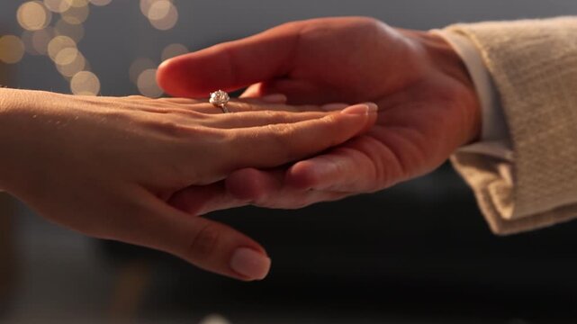 Making proposal. Man putting engagement ring on his girlfriend's finger indoors, camera moving. Bokeh effect