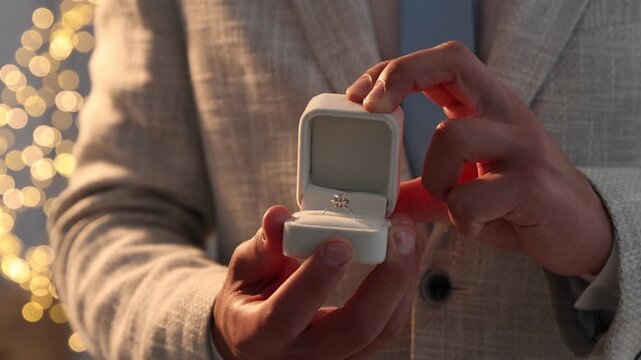 Making proposal. Man opening box with engagement ring indoors, camera moving in. Bokeh effect