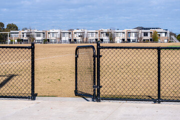 Chain link fence gate opening to grass sports field in suburban residential neighborhood of Point...