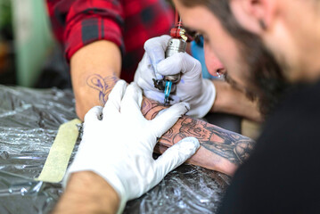 A young male bearded tattoo artist drawing a tattoo sketch on a client's forearm with a tattoo...