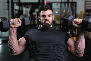 A man with a strong physique performs a bench press with dumbbells in a well-equipped gym. The atmosphere is energetic, emphasizing strength training and fitness