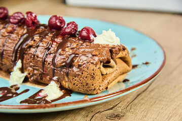A plate features chocolate rolled pancakes topped with cherries and whipped cream. The sweet dessert is presented on a blue dish, evoking appetizing indulgence