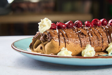 A rich chocolate rolled cake sits on a vibrant plate, adorned with fresh cherries and dollops of whipped cream. This dessert is perfect for any sweet tooth craving a delicious treat