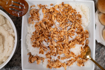  A dish of steamed rice topped with toasted almond slices and a drizzle of syrup, served alongside creamy mashed potatoes and bread rolls