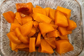 Chunks of bright orange cooked pumpkin arranged in a glass container, showcasing a vibrant color and glossy texture