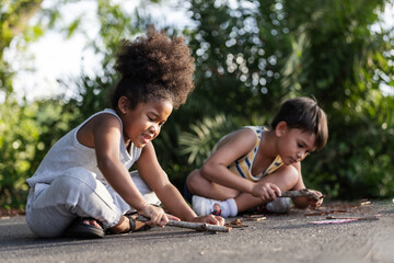 Two young children sit on the ground drawing with sticks, fully engaged in creative outdoor play....