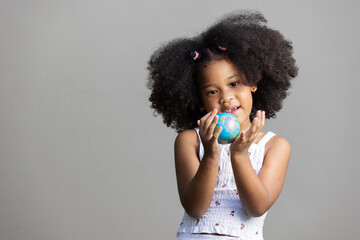 A young girl with a surprised expression holds a small globe ball in her hands. Dressed in a white...