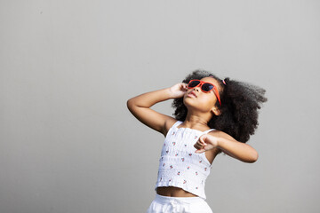 A confident young girl wearing red sunglasses looks up with flair, striking a dynamic pose. Her...