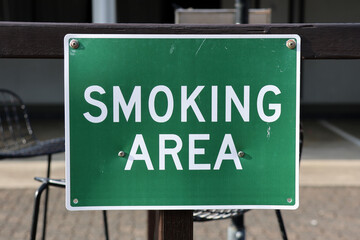Green Smoking Area sign attached to a wooden post in an outdoor lounge area