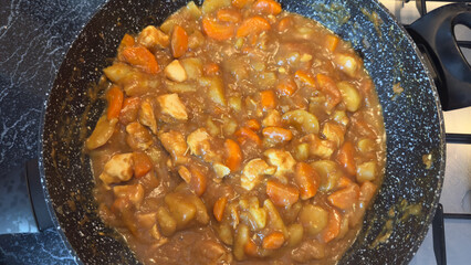 Top down of a homemade Japanese chicken and vegetable curry with carrots and potatoes simmering in a pan on a kitchen stove