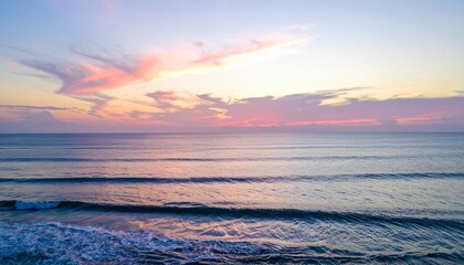 Obraz premium 穏やかな波が寄せる海岸で、柔らかなパステルカラーの空が広がる夕暮れの美しいコースタルサンセットの情景