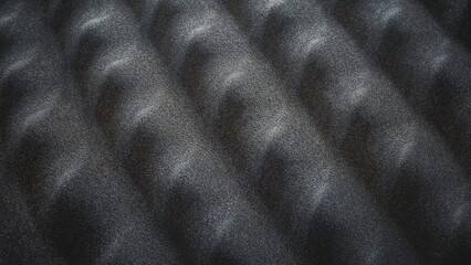 Photo of closeup of dark gray acoustic foam panel with wave pattern used for sound dampening and noise reduction in studio