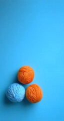 Three yarn balls, two orange, one blue, are positioned in the bottom left on a bright blue background. They cast soft shadows. The photo is well-lit with ample empty space above
