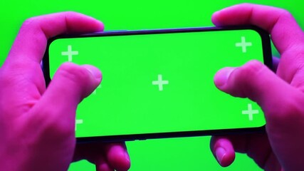 Hands holding smartphone with green screen and tracking markers, perfect for chroma key compositing. Mobile gaming or app display.