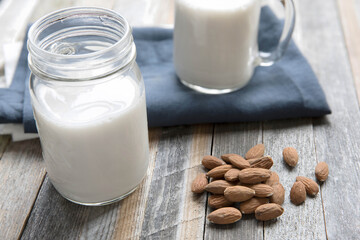 Homemade almond milk in a jar and mug with whole almonds on a rustic table. Perfect for healthy diets, organic food, and real, plant-based living