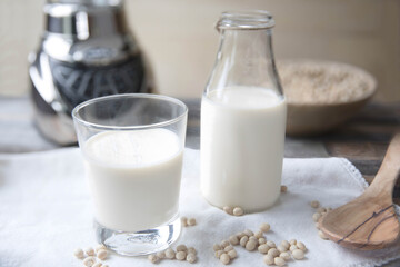 Freshly made soy milk in a glass and bottle, with soybeans and wooden spoon, perfect for organic and healthy drink themes
