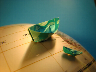 Two origami boats on a vintage globe symbolize travel, exploration, and the human journey across...