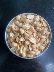 Overhead view of a bowl of roasted salted peanuts on a dark granite countertop