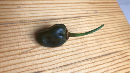 A pop of green on a wooden canvas. A pepper add a burst of color to a simple background.